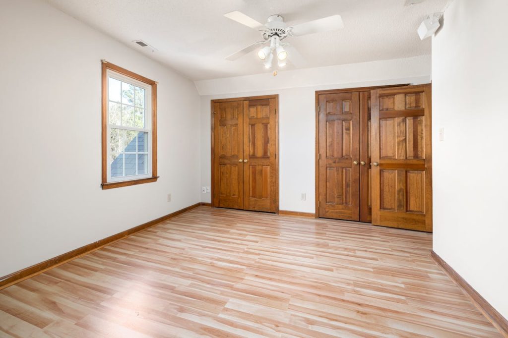 A large empty room with wooden flooring and two wooden doors, ideal for residential use.